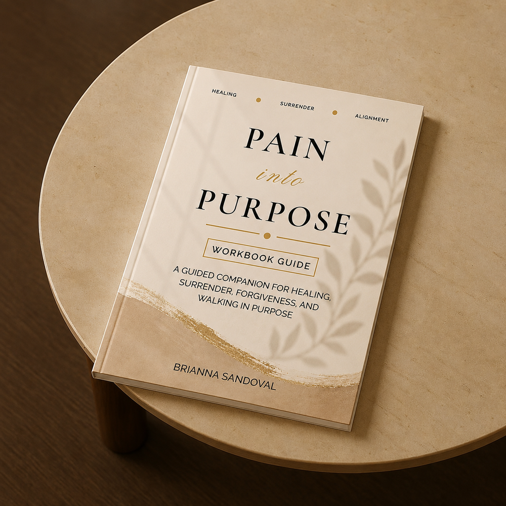 A hardcover workbook titled "Pain into Purpose" by Brianna Sandoval, placed diagonally on a round light wood table.